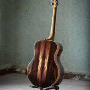 This picture shows the back of an acoustic guitar that is in a small room with a teal background. The picture shows the back of the acoustic guitar highlighting a beautiful brazilian rosewood tonewood.