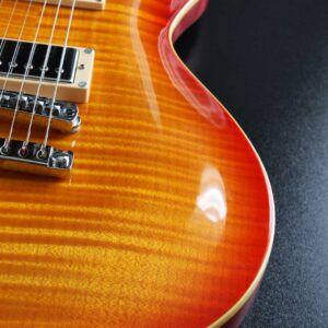 This is a close-up picture of an electric guitar. It is a Les Paul style guitar highlighting a flamed maple top. It's orange and red.