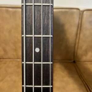 A close up shot of a bass guitar that has a Laurel fretboard. The background is a beige couch.