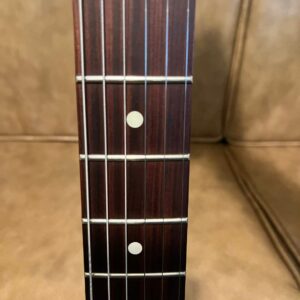 A close up shot of a bass guitar that has a Pau Ferro fretboard. The background is a beige couch.