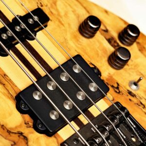 A close-up of a yellow bass guitar. This guitar has a spalted maple top that has a dark grain pattern.