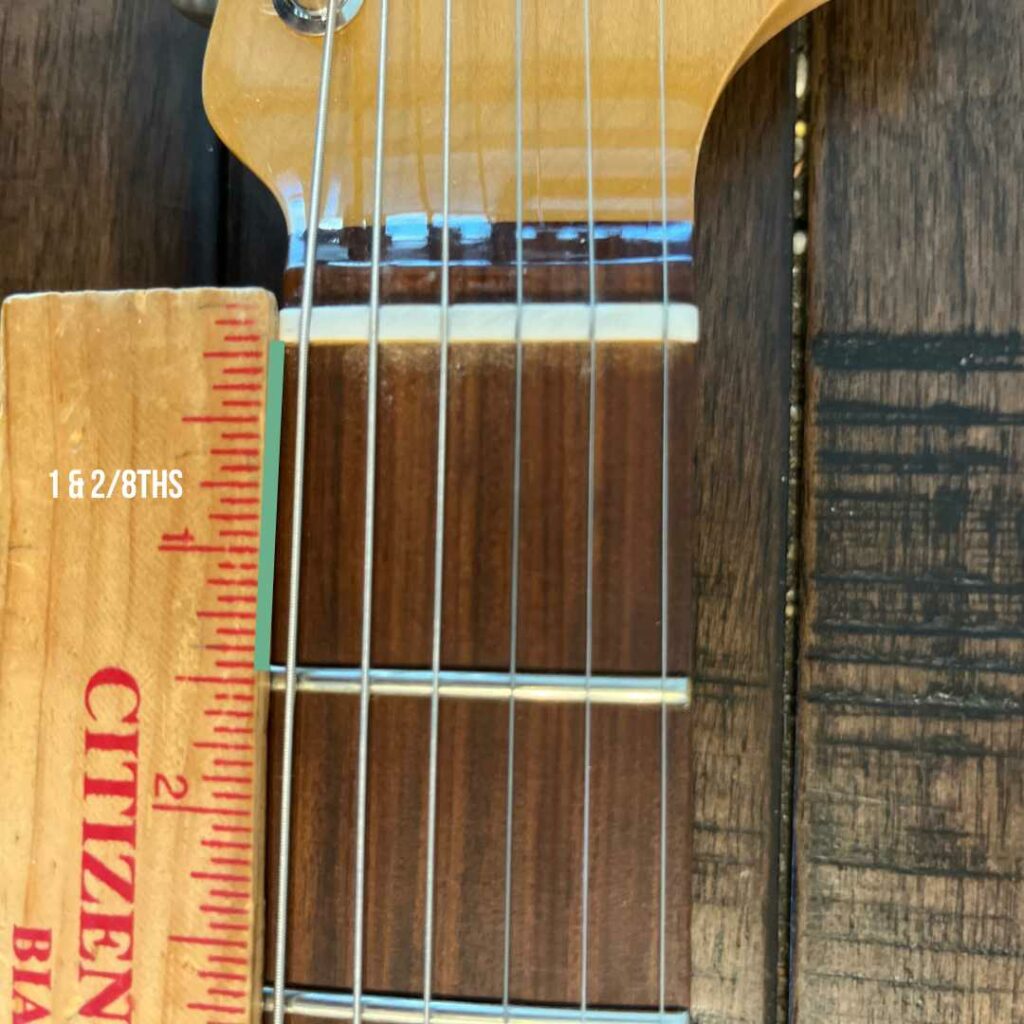 This is a picture of a guitar neck with a ruler next to it. This photo demonstrates the distance of the first fret on a electric guitar with a ruler.