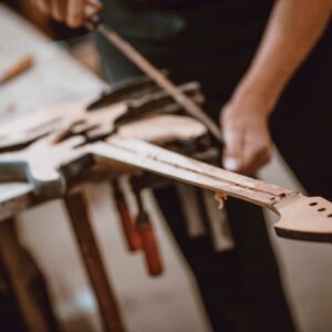 This is a picture of someone building a strat style electric guitar. The focus is on the neck of the guitar while everything else is out of focus visually.