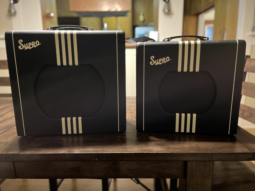 This is a picture of two black Supro Delta King amps with a cream stripe. They are next to each other on a hardwood tabl.