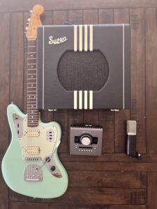 This is an overhead shot of a black and cream Supro Delta King with a Seafoam Green Fender Jaguar, black Universal Audio Apollo Twin X, and a condenser microphone. This is showing the gear that was used for te audio samples of the Delta King.