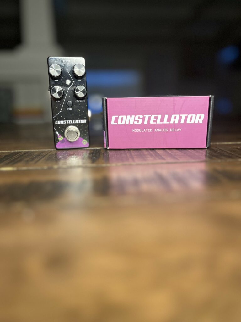 An original picture of the Pigtronix Constellator mini guitar pedal sitting next to it's packaging on a hardwood table.