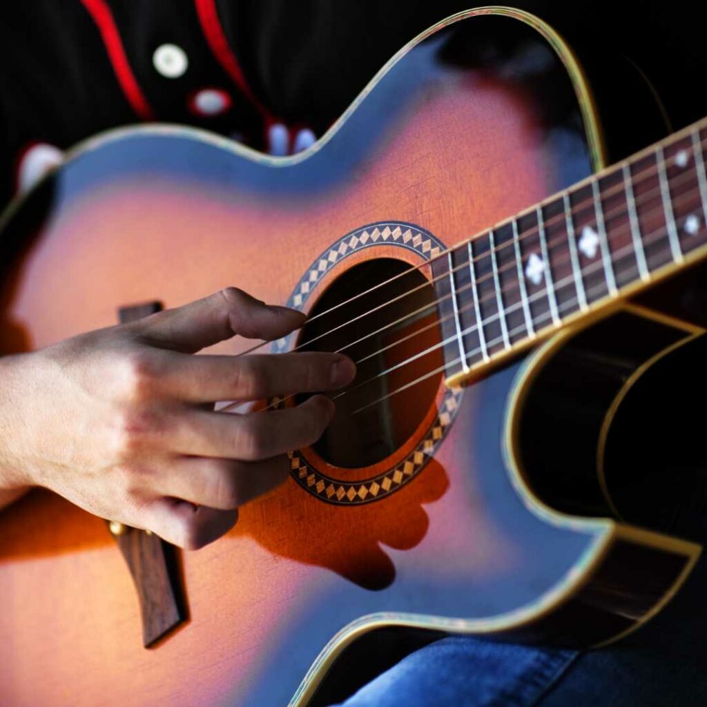 This is a close up photograph of an acoustic guitar with a florentine cutaway. There is a hand strumming the acoustic guiitar.