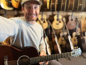 This is a picture of Brad Johnson, the Founder and Writer of Song Production Pros testing out a Guild M-20 all mahogany top guitar. He is wearing a blue sweatshirt and green hat.