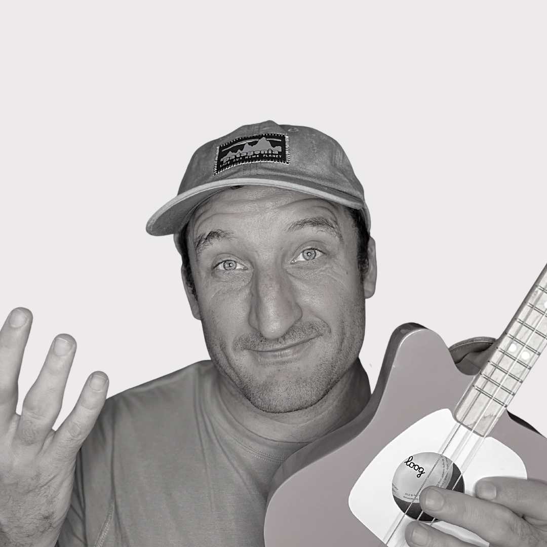 This featured image of the review article, "Loog Guitar Review" shows a black and white photo of the founder/writer of Song Production Pros, Brad Johnson, holding a pink Loog Mini.