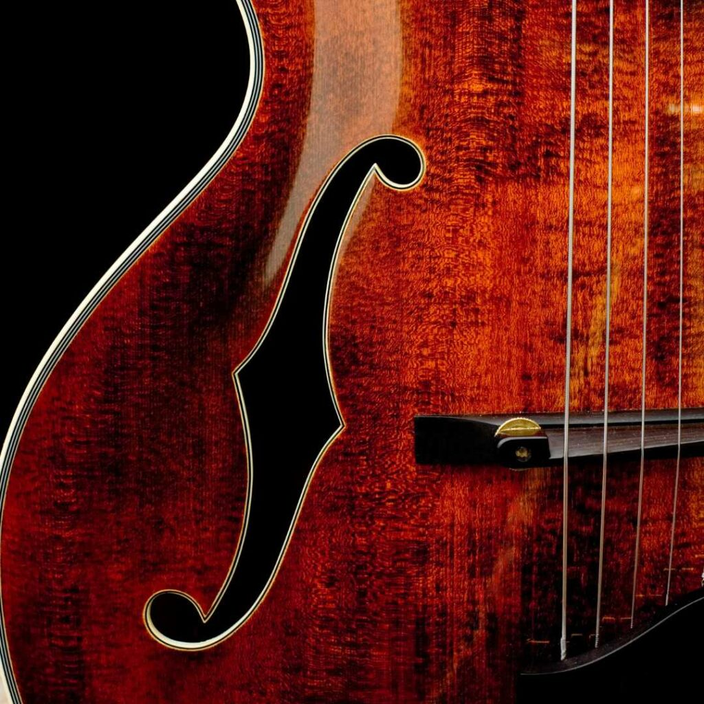 This is a picture of an archtop guitar that features an F-Hole sound hole in the body. The photo is a close up shot of the f-hole and the guitar is a dark red color.